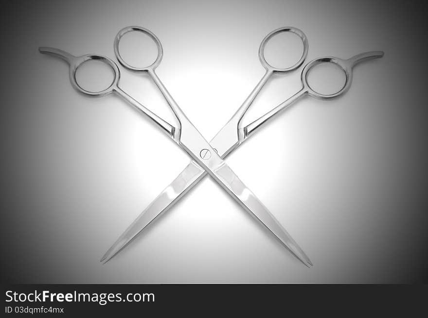 Two stainless steel hairdressing scissors overlapping each other against a white and grey light effect background. Two stainless steel hairdressing scissors overlapping each other against a white and grey light effect background