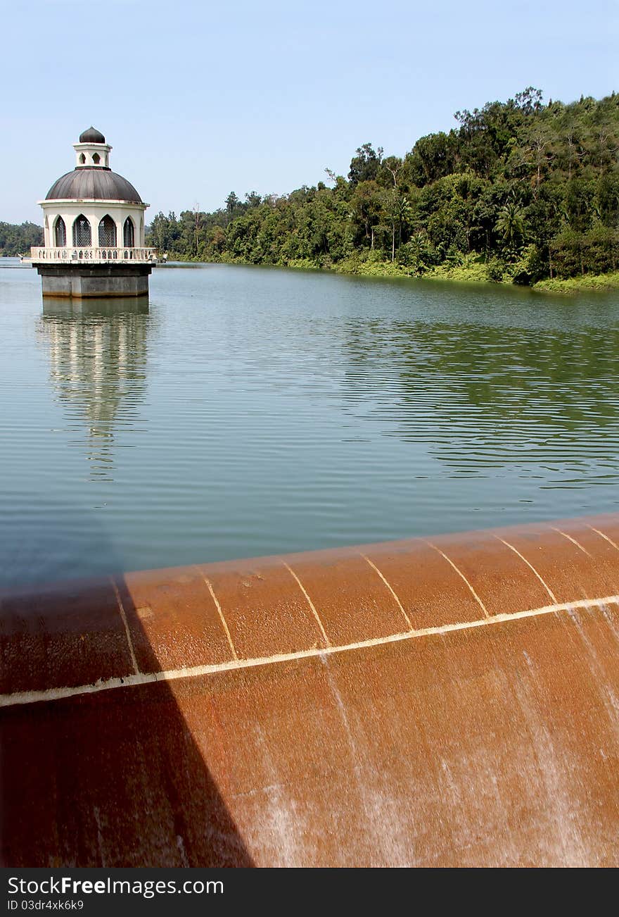 Raw water reservoir with intake tower and dam in the foreground. Water has reached and passed the top level of the dam and thus overflowing back to downstream river. Raw water reservoir with intake tower and dam in the foreground. Water has reached and passed the top level of the dam and thus overflowing back to downstream river.