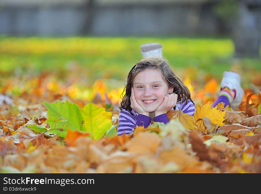 Smiling little girl laying on autumn leaves