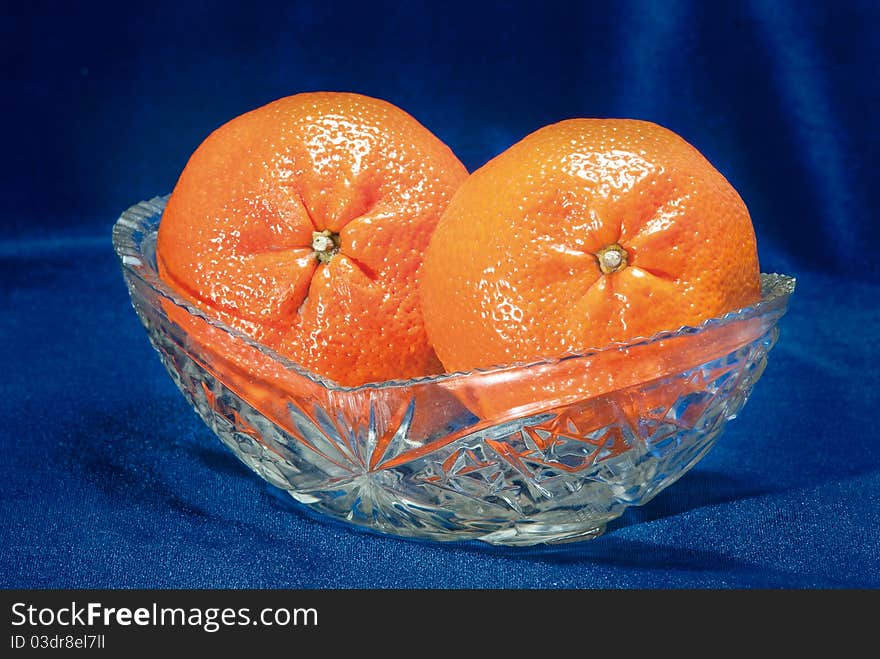 Two tangerines in a glass vase on a dark blue background. Two tangerines in a glass vase on a dark blue background