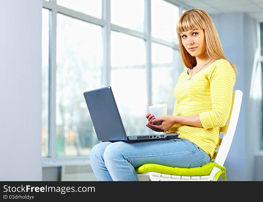 Casual girl sitting on the chair with notebook and holding a cup. Casual girl sitting on the chair with notebook and holding a cup