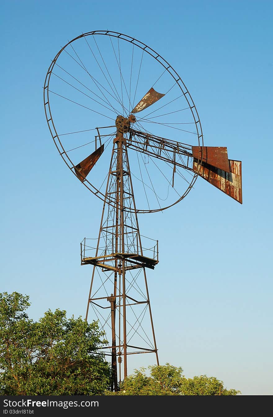 Old rusted windmill over green trees. Old rusted windmill over green trees