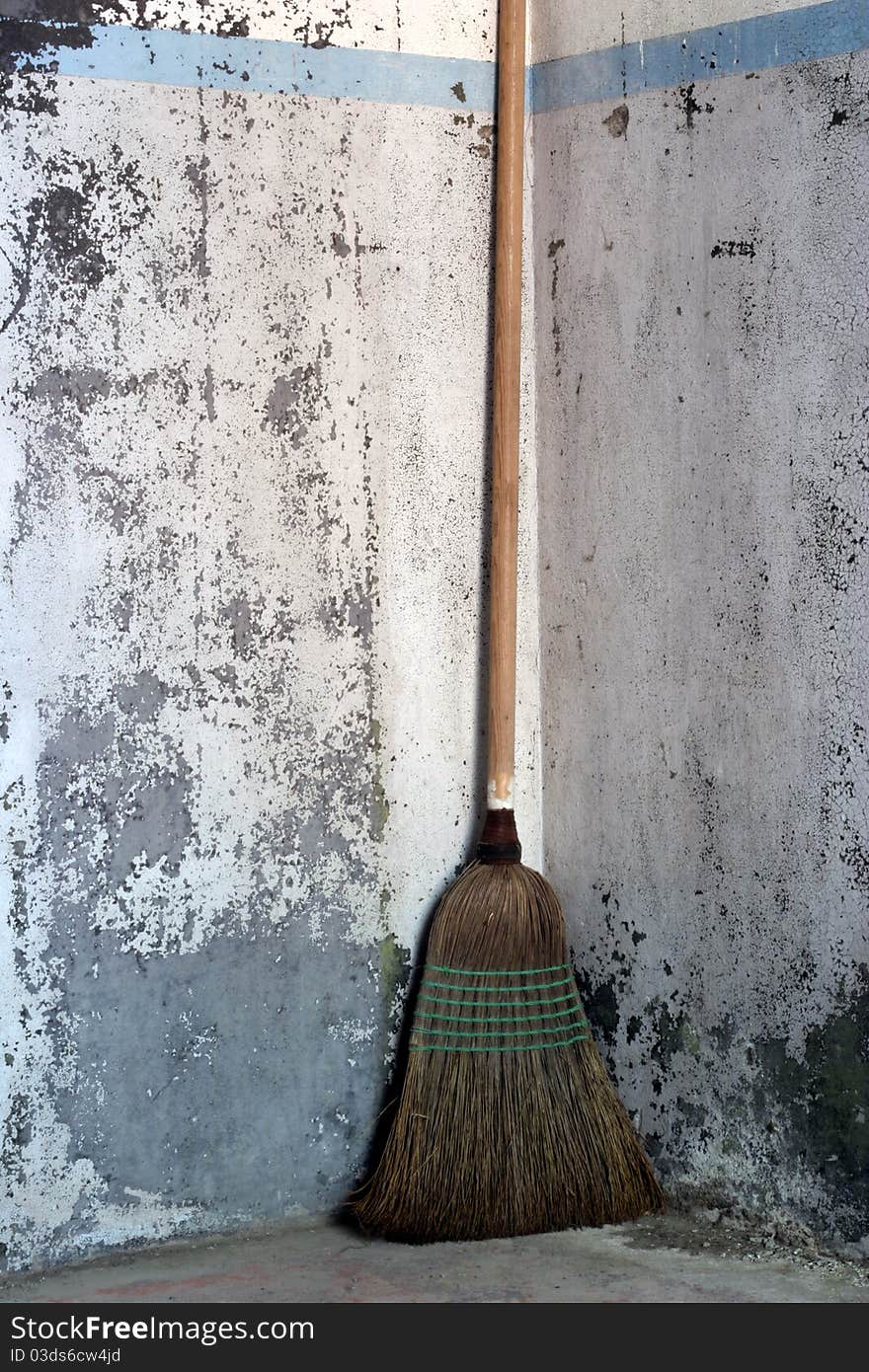 A corn brrom standing in a weathered concrete corner with old, heavily textured, cracked and peeling paint. A corn brrom standing in a weathered concrete corner with old, heavily textured, cracked and peeling paint.