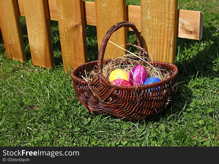 Some coloured easter eggs lying in a basket in front of a wooden fence