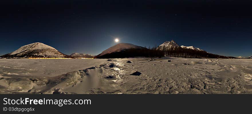 Panorama moonlight from sea ice in the winter with mountains and reflection in the ice