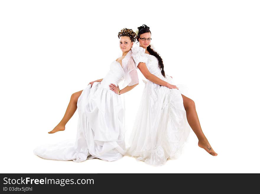 Two young beautiful brides is showing off their legs in wedding dress on white isolated background. Two young beautiful brides is showing off their legs in wedding dress on white isolated background.