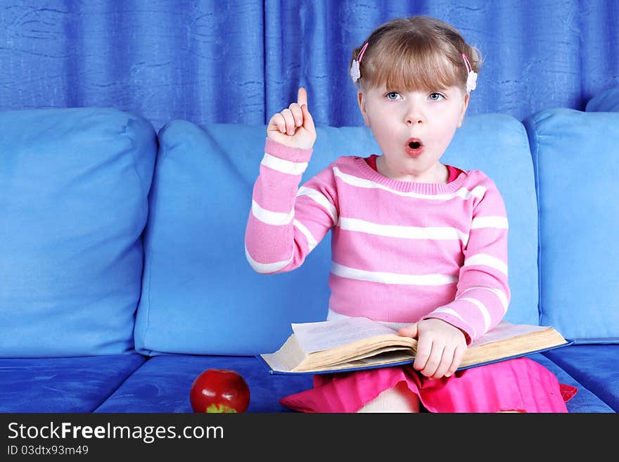 Surprised little girl with apple and books in sofa