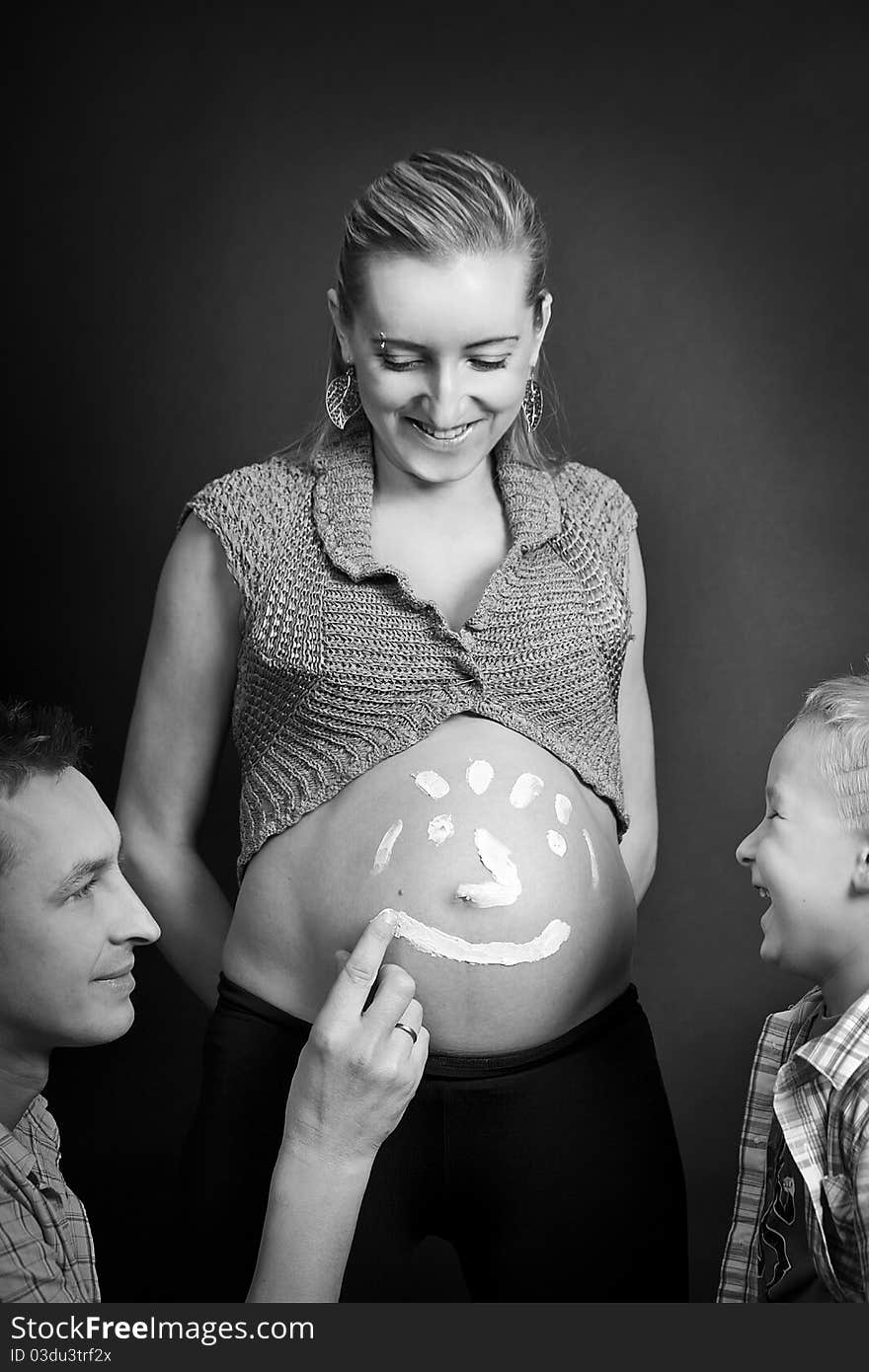 Dad and son painting funny face on mummys pregnant belly. Dad and son painting funny face on mummys pregnant belly