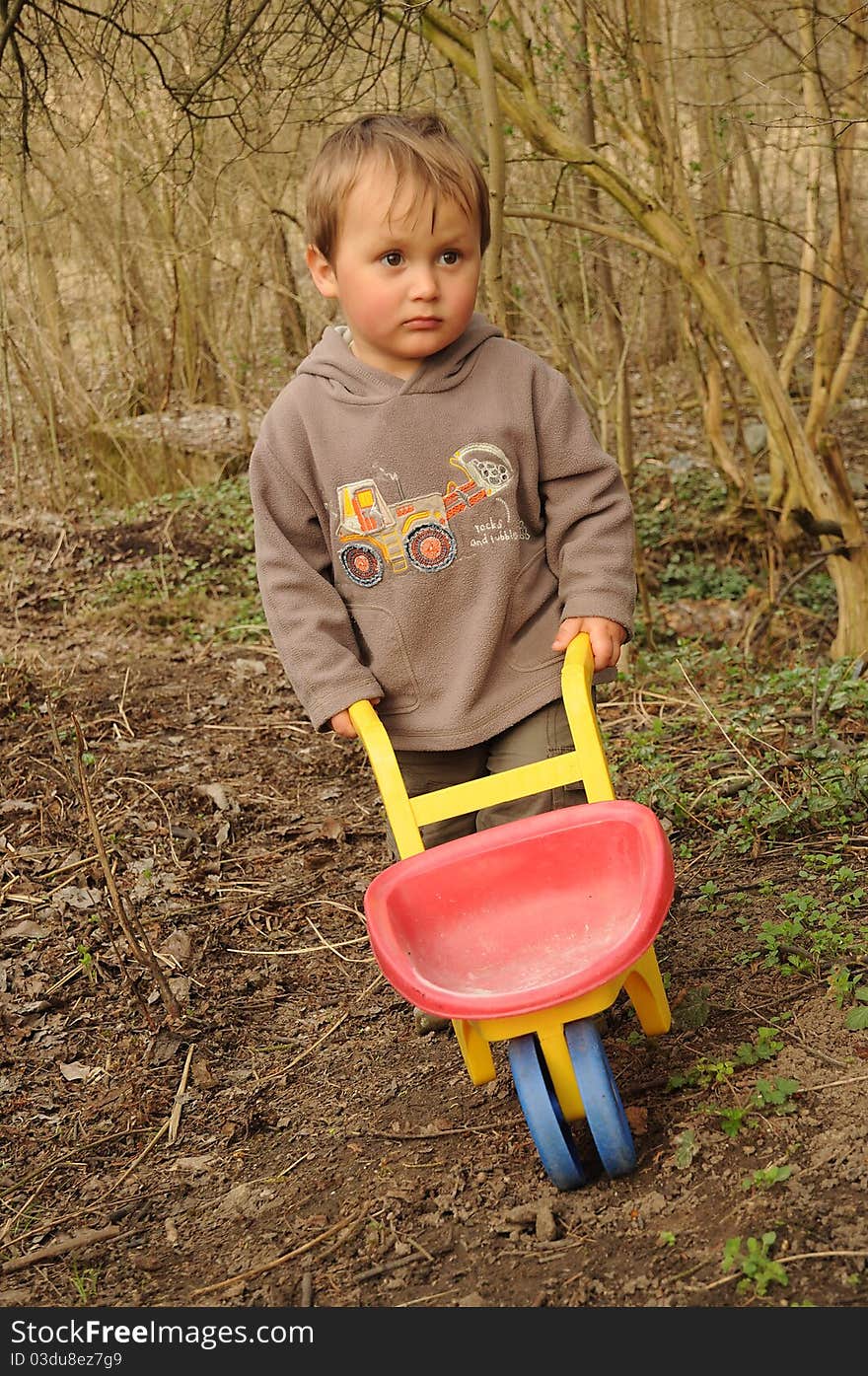 Little boy with an empty  wheelbarrow working in a desolate garden. Little boy with an empty  wheelbarrow working in a desolate garden