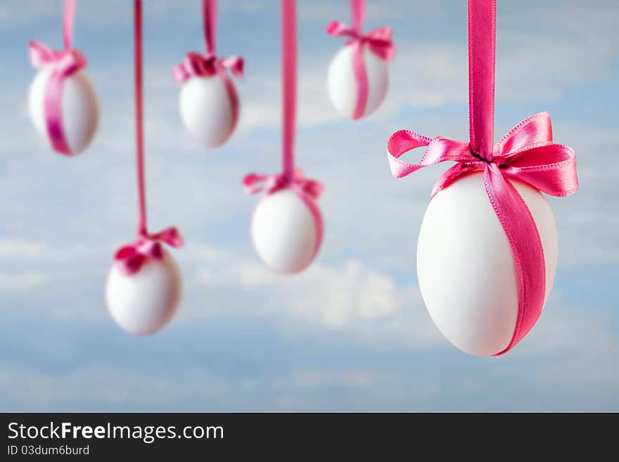 Six white easter eggs hanged on the pink satin ribbons on the blue sky background. Six white easter eggs hanged on the pink satin ribbons on the blue sky background