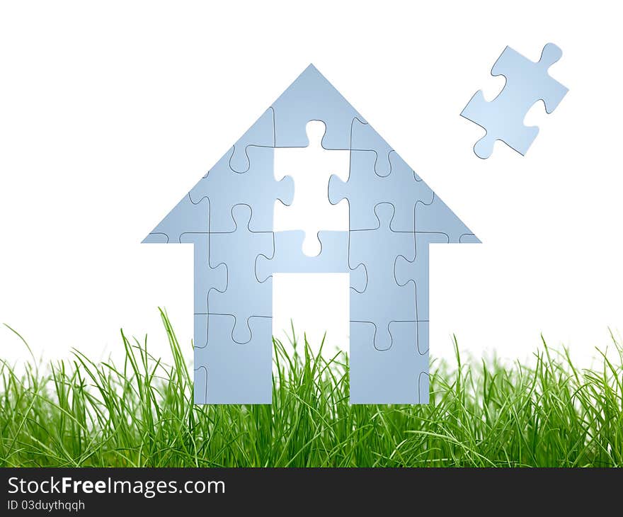 A jigsaw house on green grass siolated against a white background. A jigsaw house on green grass siolated against a white background