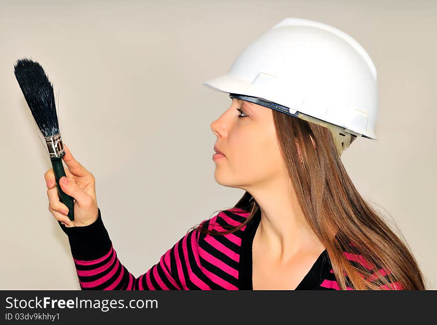 A girl in a white helmet, holding a paintbrush against the wall. A girl in a white helmet, holding a paintbrush against the wall