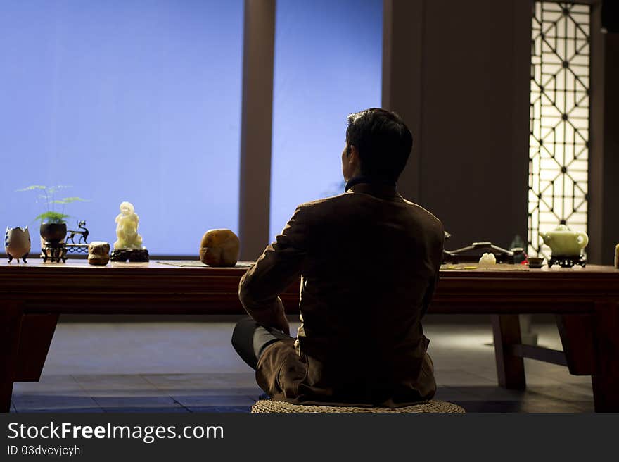 A Chinese meditating before jade on table. A Chinese meditating before jade on table