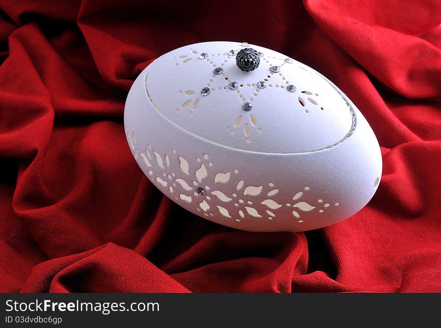 Decorative casket from a goose egg rests against a red background