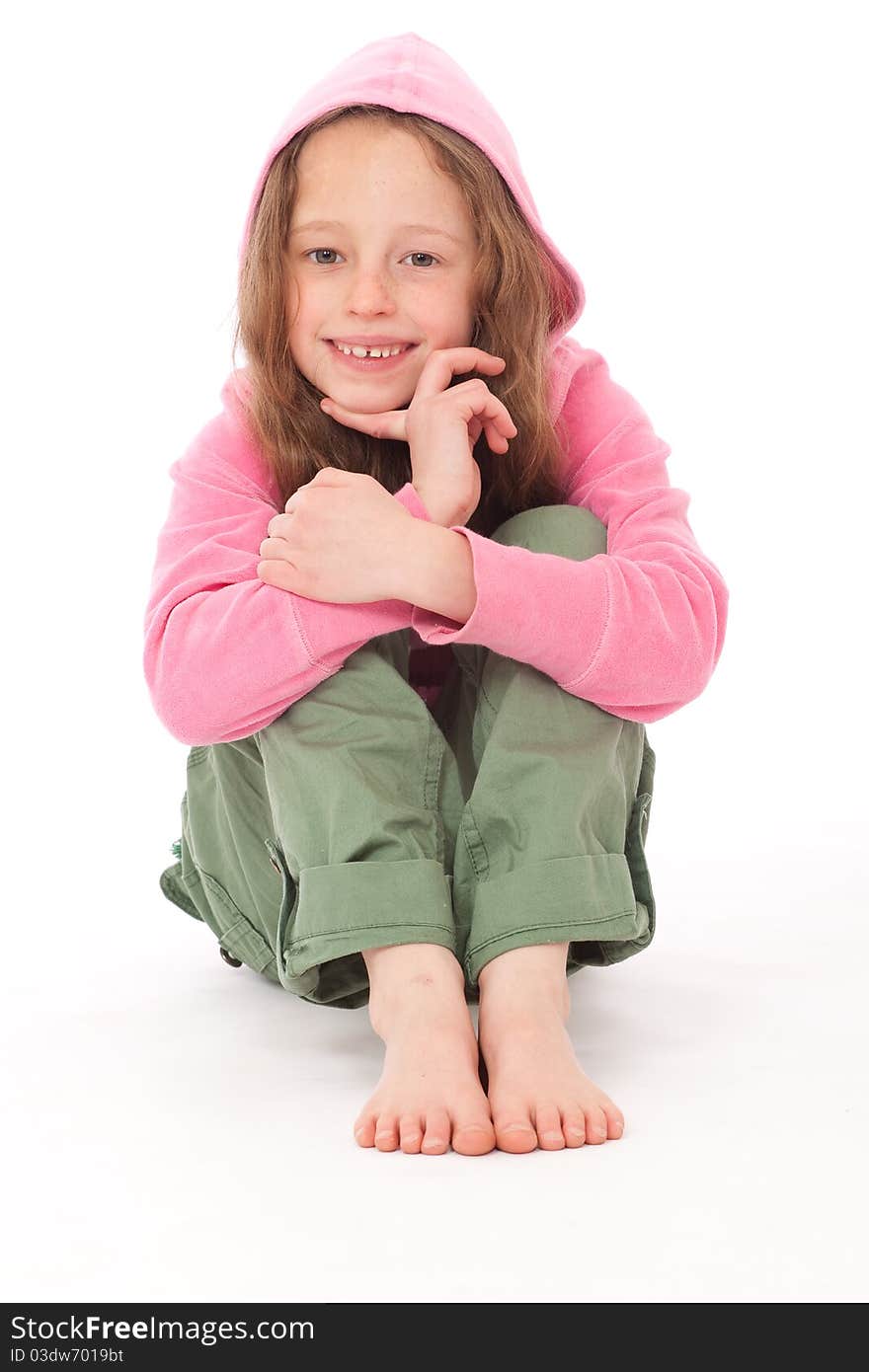 Young girl in pink hood top and green trousers sitting on floor and smiling. Young girl in pink hood top and green trousers sitting on floor and smiling