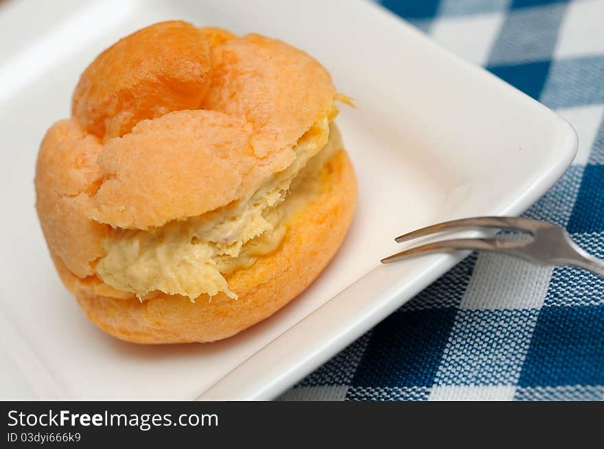 Closeup shot of single freshly baked cream puff on white plate. Closeup shot of single freshly baked cream puff on white plate.