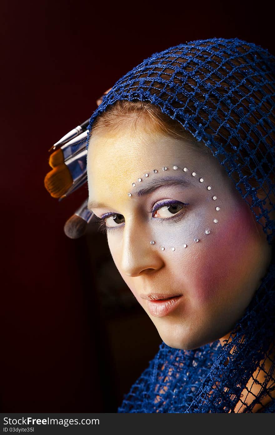 Close up portrait of a beautiful woman with artistic make-up decorated with crystals and brushes for makeup in a lightweight scarf