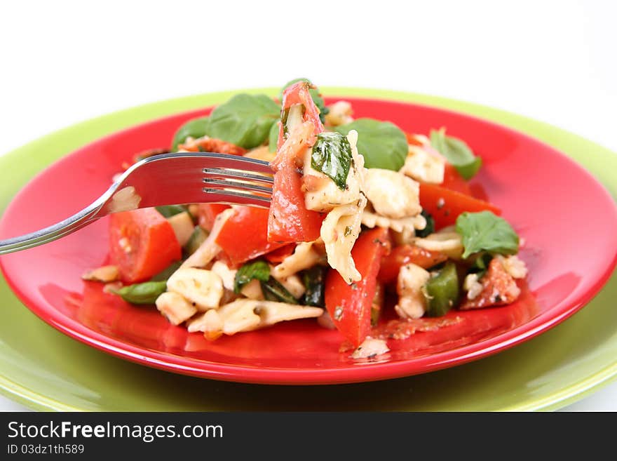 Salad - made of farfalle pasta, tomato, salami, bell pepper and mozzarella, decorated with basil, being eaten with a fork. Salad - made of farfalle pasta, tomato, salami, bell pepper and mozzarella, decorated with basil, being eaten with a fork