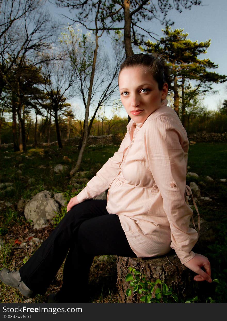 Pregnancy in nature, beautiful young and pregnant women in forest sitting on stump