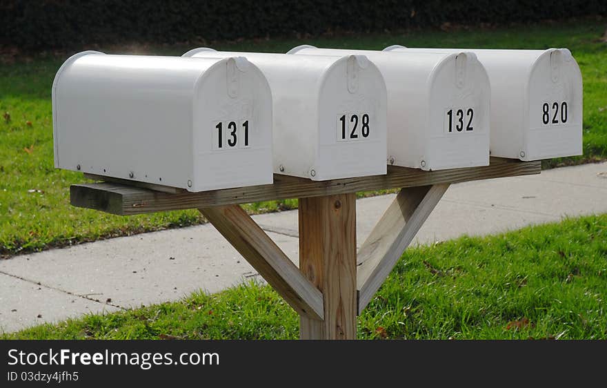 Four white mailboxes on a wooden post with green grass and sidewalk. Four white mailboxes on a wooden post with green grass and sidewalk.