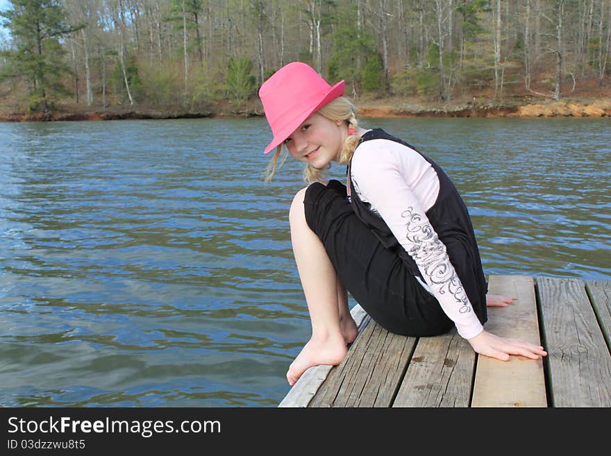 Young girl in a pink hat sitting on the edge of a dock. Young girl in a pink hat sitting on the edge of a dock.