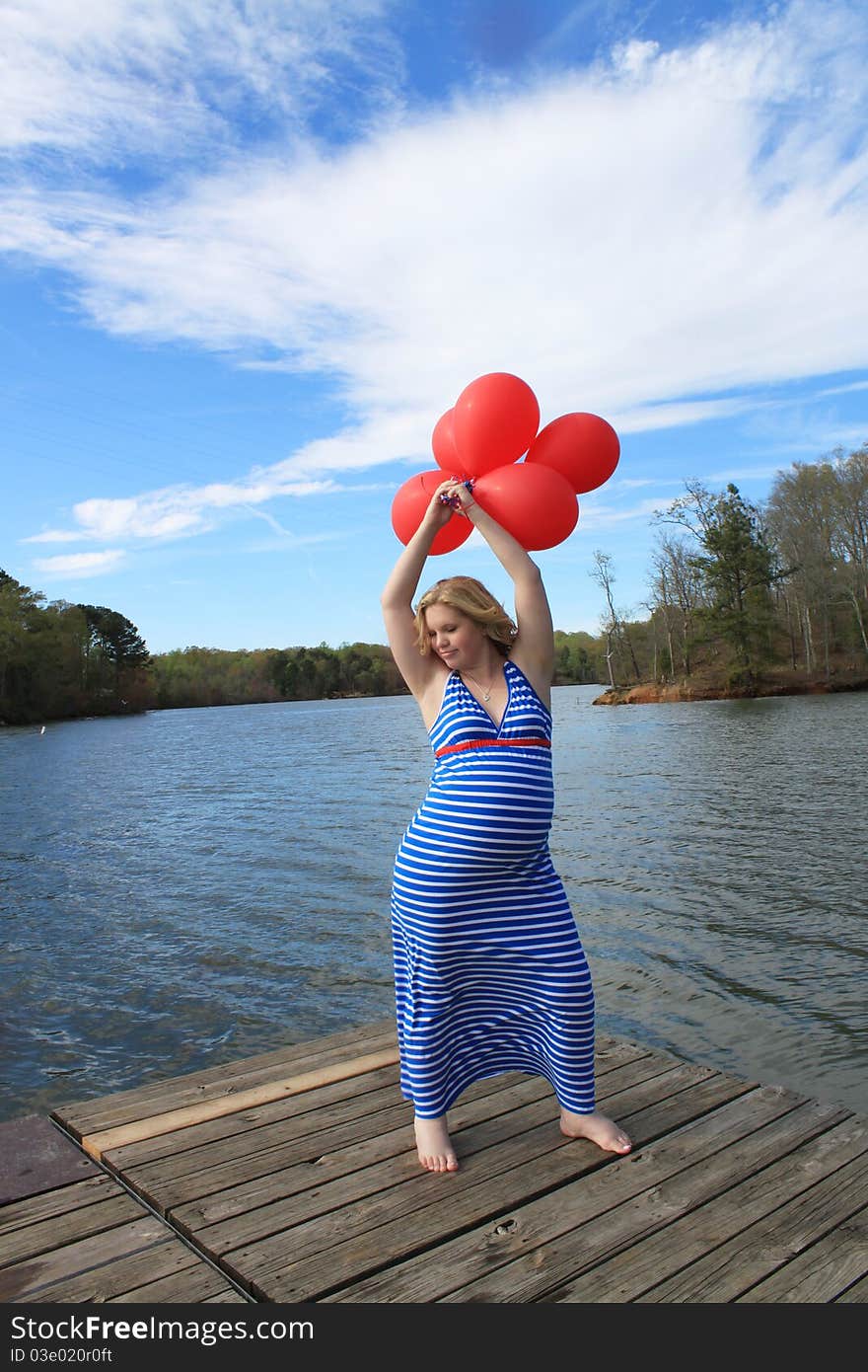 Pregnant woman on a dock holding a bunch of red balloons above her head. Pregnant woman on a dock holding a bunch of red balloons above her head.