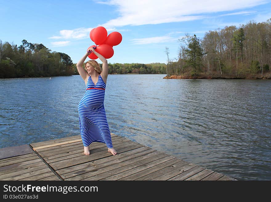 Beautiful happy pregnant woman holding balloons on the dock in a beautiful natural setting. Beautiful happy pregnant woman holding balloons on the dock in a beautiful natural setting.