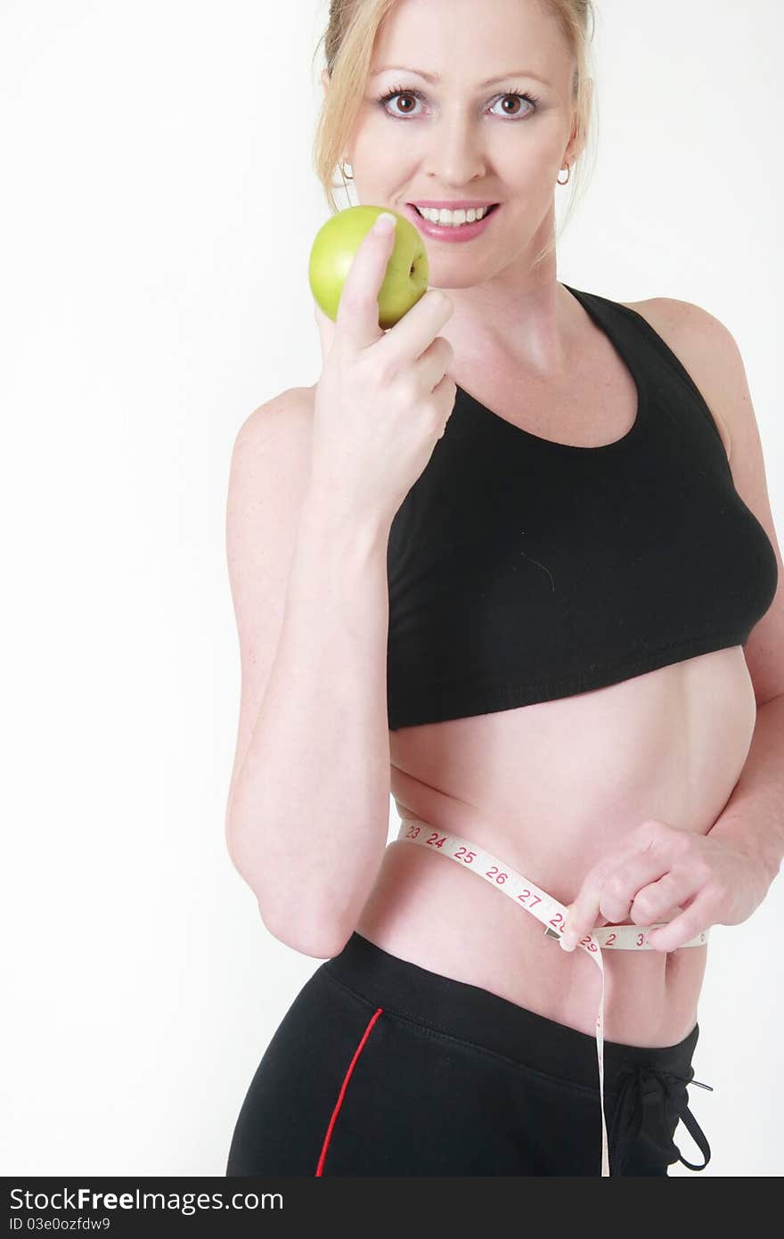 Attractive blond caucasian woman smiling wearing fitness attire holding an apple with measuring tape around thin waist. Attractive blond caucasian woman smiling wearing fitness attire holding an apple with measuring tape around thin waist