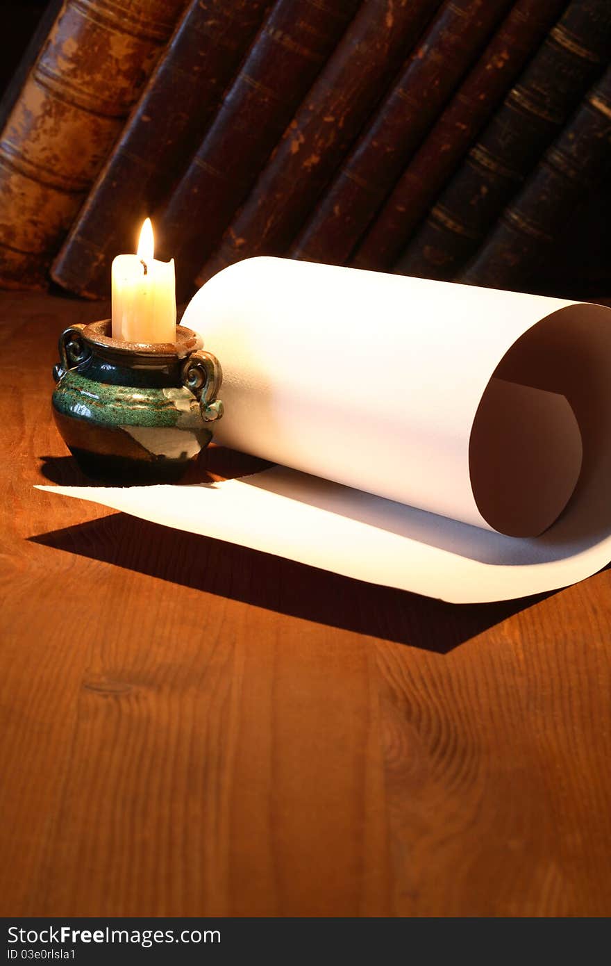 Old paper near lighting candle and stack of vintage books on wooden surface. Old paper near lighting candle and stack of vintage books on wooden surface