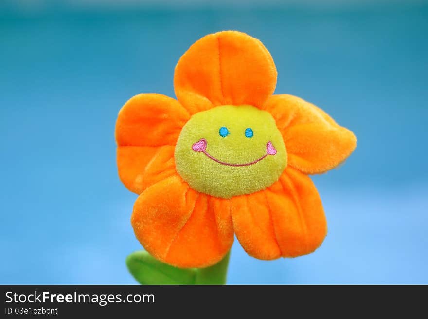 A happy, smiling bright orange and yellow toy flower with the turquoise blue water of a pool as the background. A happy, smiling bright orange and yellow toy flower with the turquoise blue water of a pool as the background