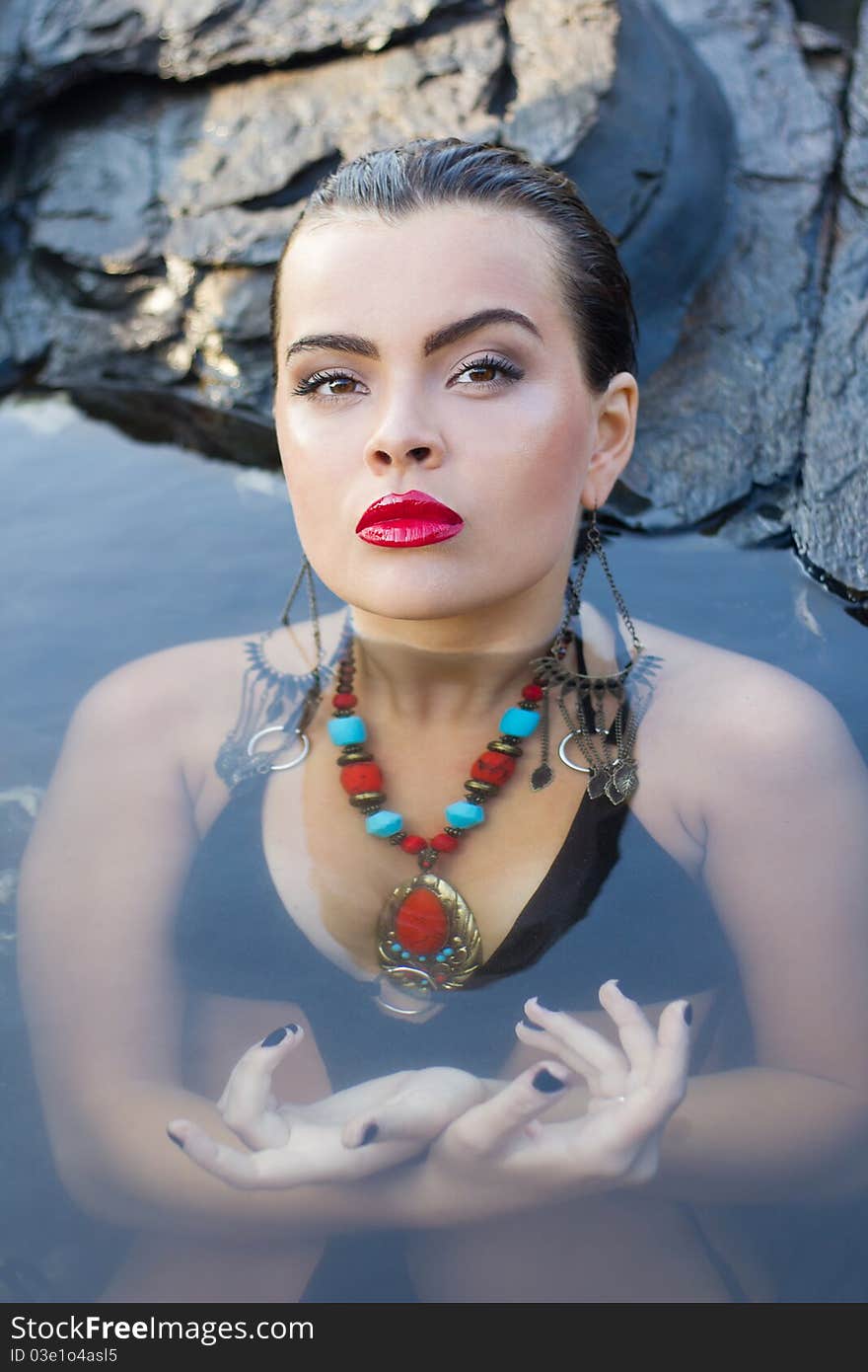 Glamorous brunette with bright makeup and accessories resting at a rock spa. Glamorous brunette with bright makeup and accessories resting at a rock spa