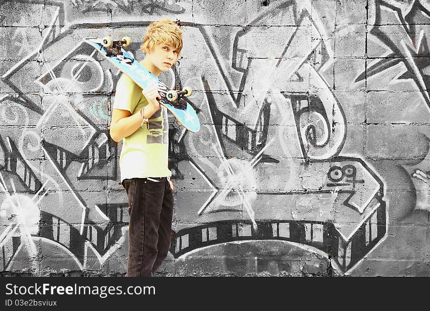 A boy with a skateboard in an urban setting with black and white graffiti in the background. A boy with a skateboard in an urban setting with black and white graffiti in the background