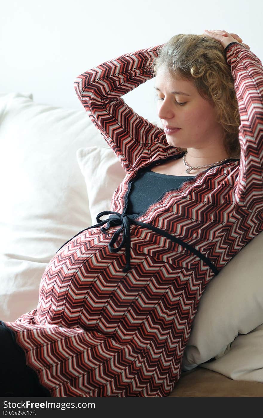 Young prengnant woman sitting an watching her abdomen. Young prengnant woman sitting an watching her abdomen.