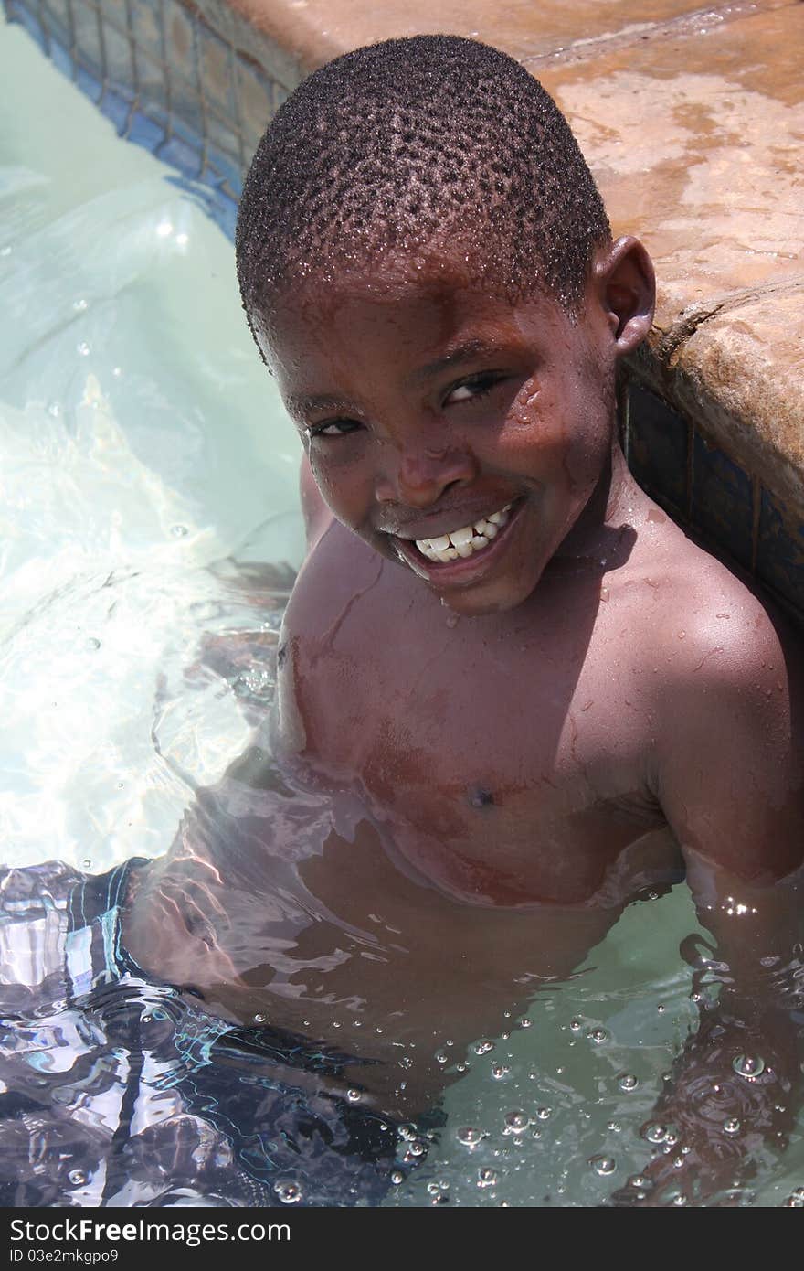 Young black african boy sitting on steps of swimming pool. Young black african boy sitting on steps of swimming pool