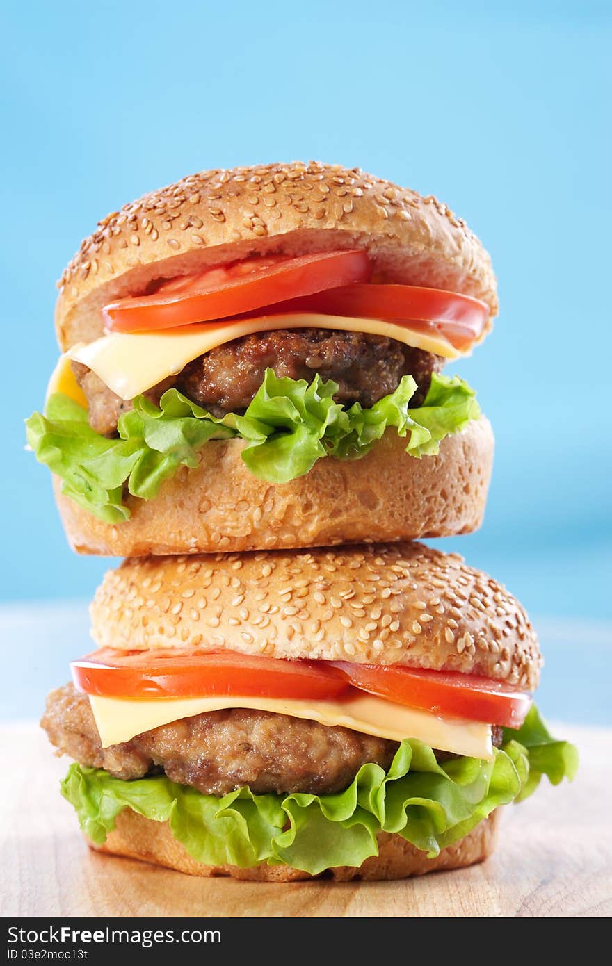 Two cheeseburgers with tomatoes and lettuce on a wooden table with blue background