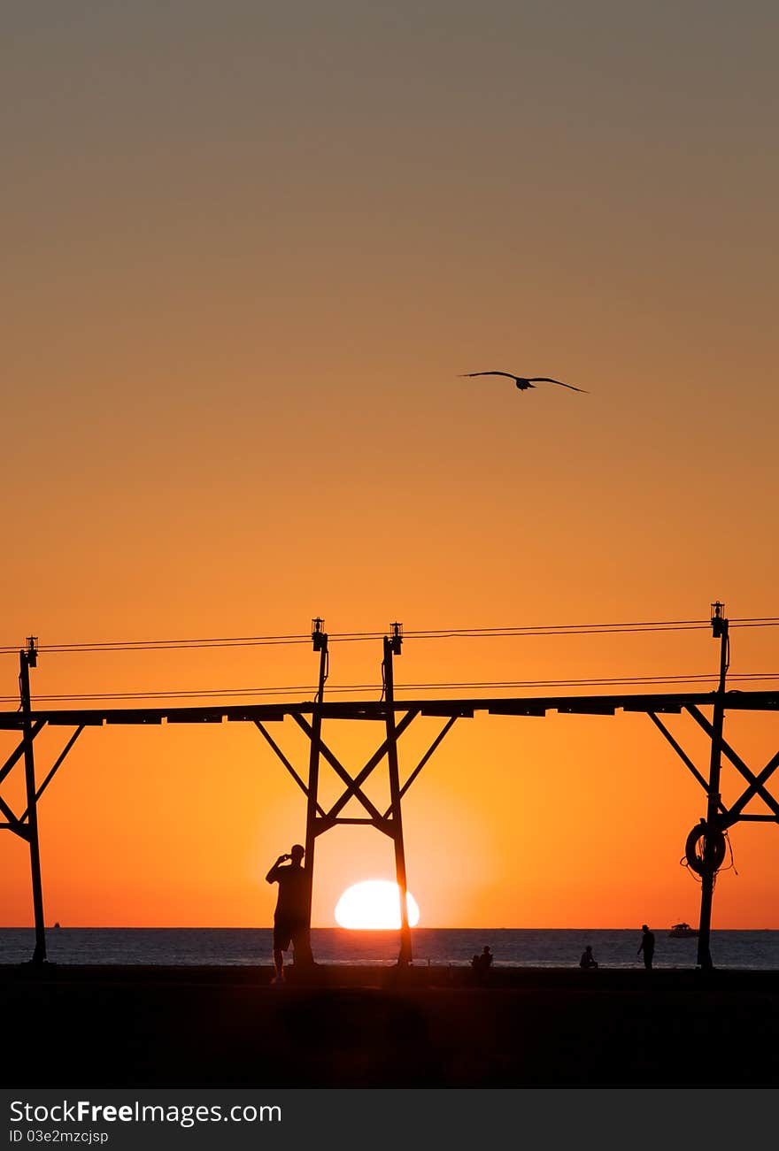 People silhouetted by the sunset as they walk on a pier in Lake Michigan. People silhouetted by the sunset as they walk on a pier in Lake Michigan