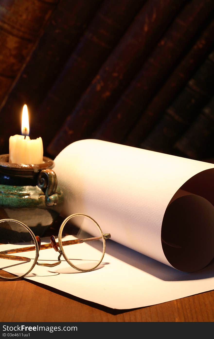 Scroll and old spectacles near lighting candle on dark background with vintage books. Scroll and old spectacles near lighting candle on dark background with vintage books