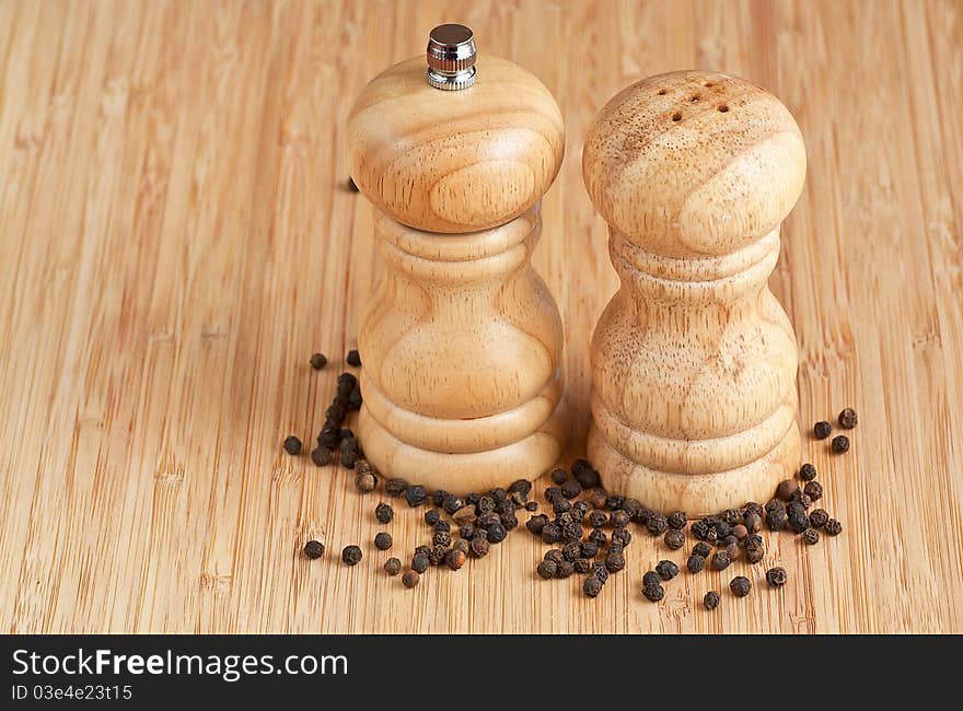 Salt and pepper grinders on a table, with pepper spread around