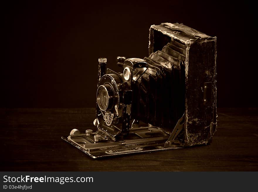 Old bellows camera in sepia on the black background. Old bellows camera in sepia on the black background