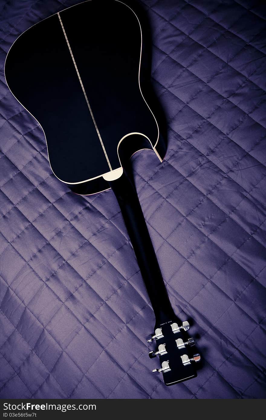 Black shiny acoustic guitar on bed. Black shiny acoustic guitar on bed