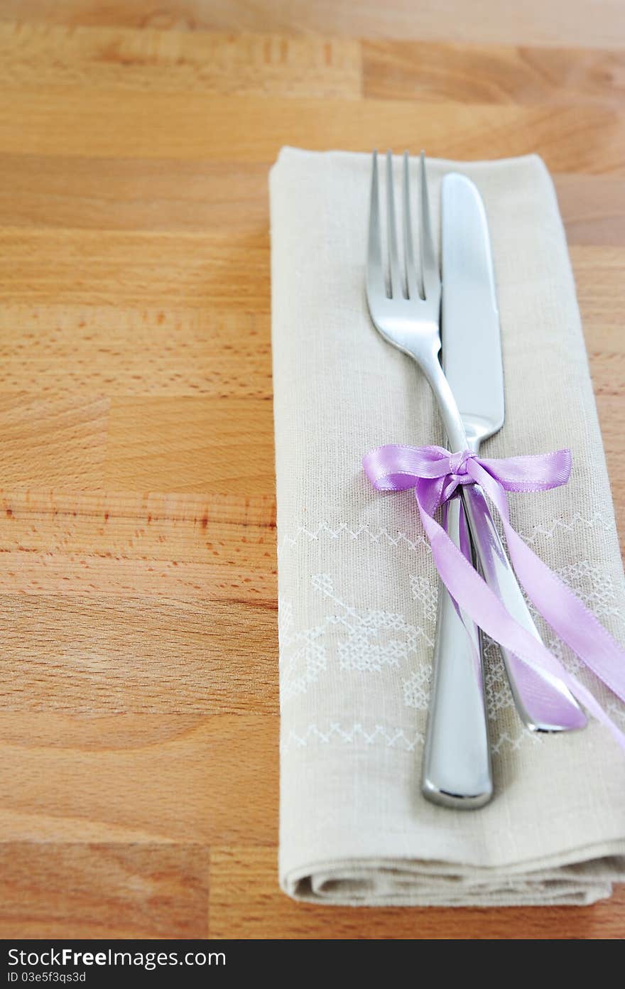 Fork and knife, tied with purple ribbon, with a linen cloth on a wooden table. Fork and knife, tied with purple ribbon, with a linen cloth on a wooden table