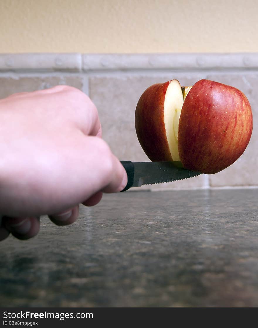 Red apple being cut in half with a sharp knife being held up by one single toothpick