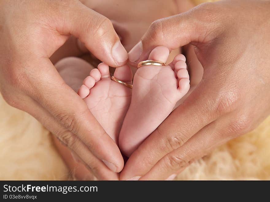 A father holding his baby's feet with fingers showing a heart shape, the baby's toes has it's parents wedding bands on. A father holding his baby's feet with fingers showing a heart shape, the baby's toes has it's parents wedding bands on.