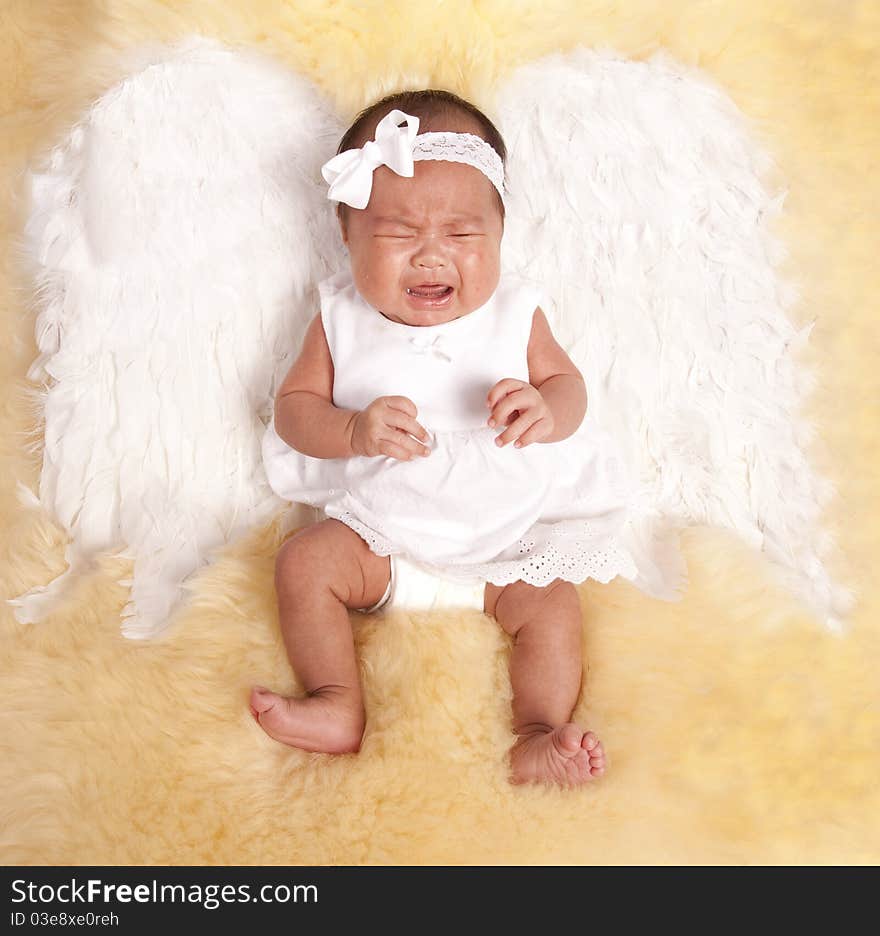 A beautiful oriental baby laying on a fur rug with her white angel wings on her back, with a sad expression on her face. A beautiful oriental baby laying on a fur rug with her white angel wings on her back, with a sad expression on her face.