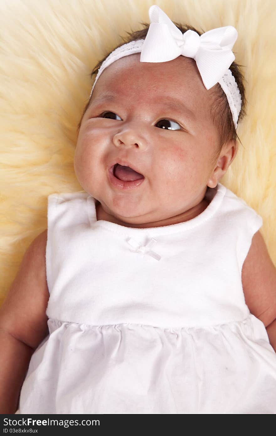 A beautiful oriental baby in her beautiful white dress laying down on a rug with a sweet expression on her face. A beautiful oriental baby in her beautiful white dress laying down on a rug with a sweet expression on her face.