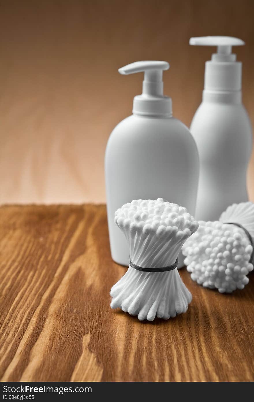 Cotton swabs and bottles on brown wooden board