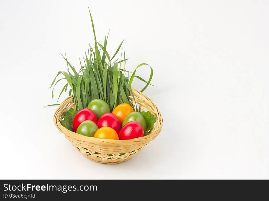 Colored eggs on grass and leaf in basket on white background. Colored eggs on grass and leaf in basket on white background.