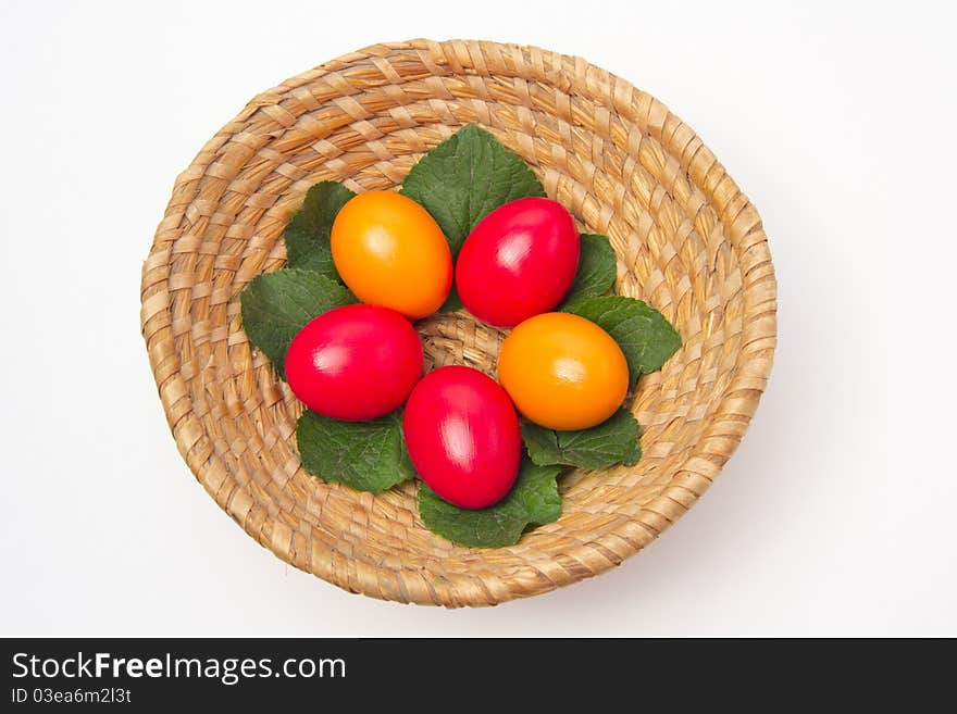 Red and yellow eggs laying on leafs in a basket on white background. Red and yellow eggs laying on leafs in a basket on white background.