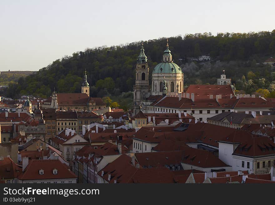 View over rooftops of Little Quarter historical part of Prague, Czech Republic. In view: Baroque St. Michaels church and Petrin hill, summer house in US Embassy gardens in upper right. View over rooftops of Little Quarter historical part of Prague, Czech Republic. In view: Baroque St. Michaels church and Petrin hill, summer house in US Embassy gardens in upper right.