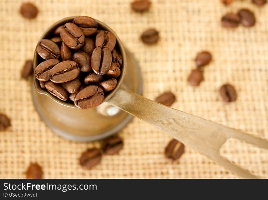 Coffee beans in a coffee pot on burlap sack background